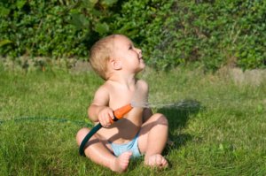 Baby mit Gartenschlauch für Regenwasser
